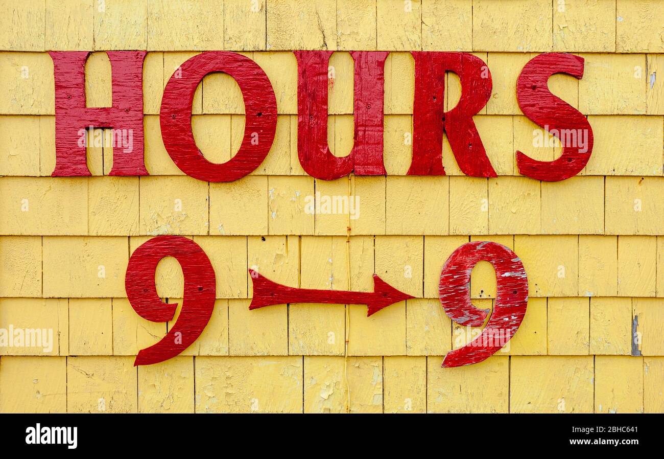 Schild mit Öffnungszeiten auf Seagull's Nest Gift Shop façade. Rot lackierte Buchstaben auf gelb lackiertem Schindelgleis. North Rustico Harbour, PEI, Kanada Stockfoto