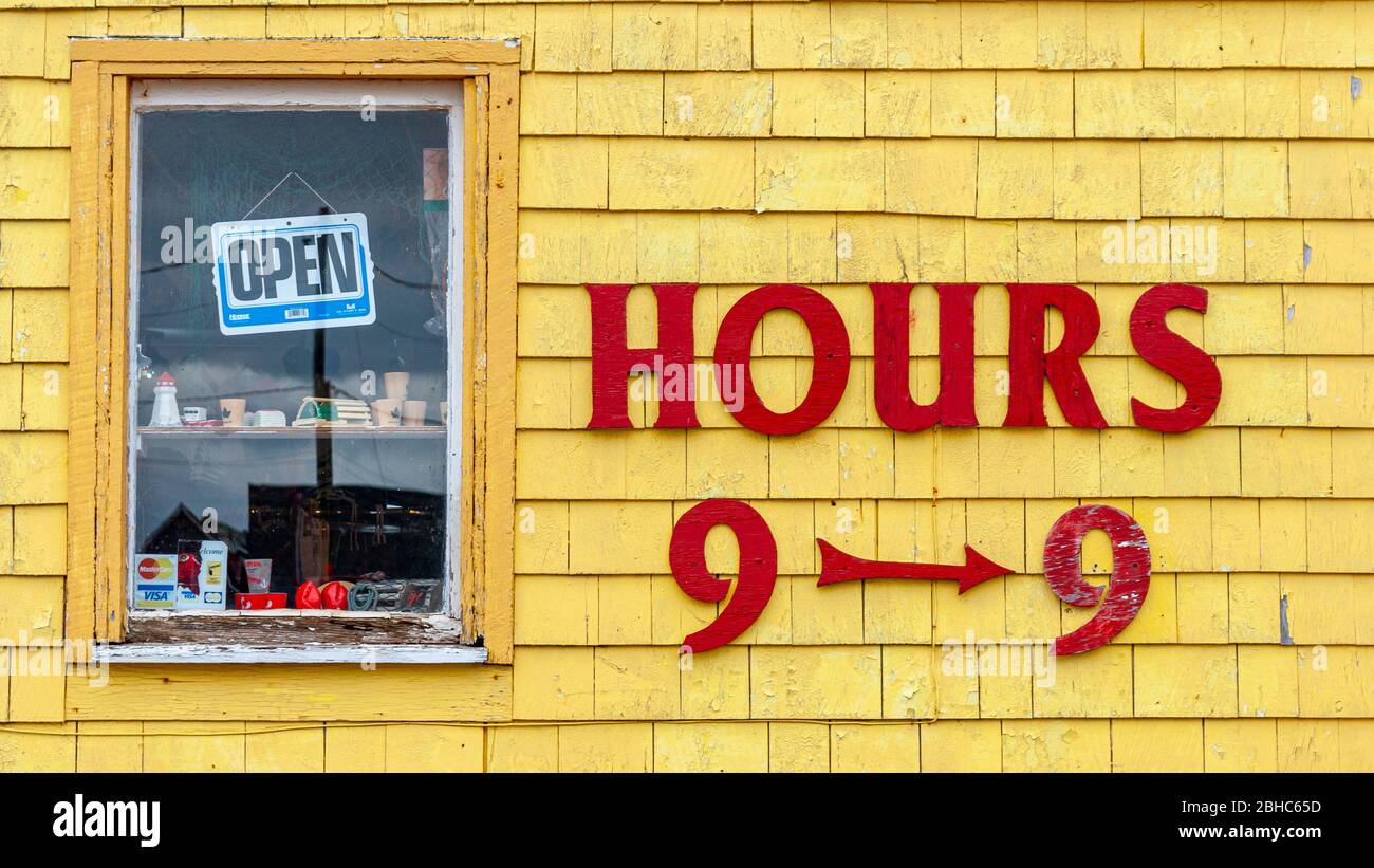 Öffnungszeiten gepostet auf Seagull's Nest Gift Shop façade. Rote Buchstaben auf gelb bemalten Schindeln. Fenster mit dem Schild „Öffnen“. North Rustico Harbour, PEI, CA Stockfoto
