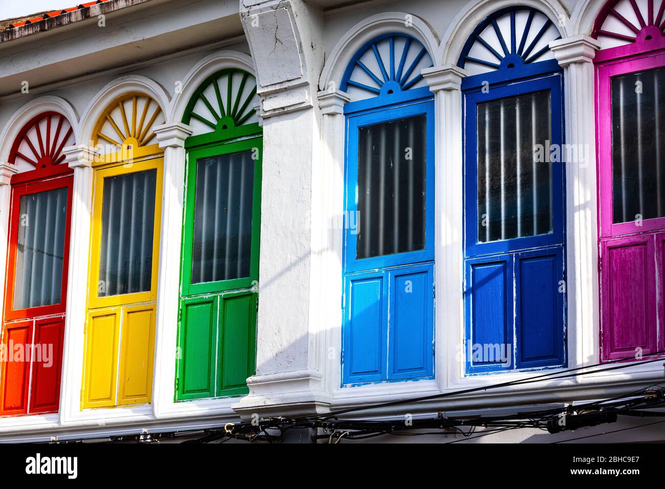 Sechs farbige Türen oder Fenster draußen an der Fassade eines alten Hauses in Phuket in Thailand. Rot, gelb und grün auf Gebäude mit weißer Wand. Stockfoto