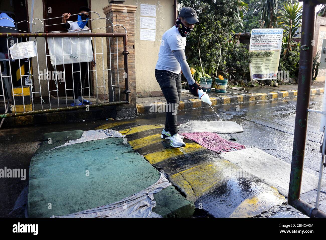 Antipolo City, Philippinen - 22. April 2020: Dorfsicherheitswache gießen Wasser mit Desinfektionslösung am Eingangstor, um Füße und V zu desinfizieren Stockfoto