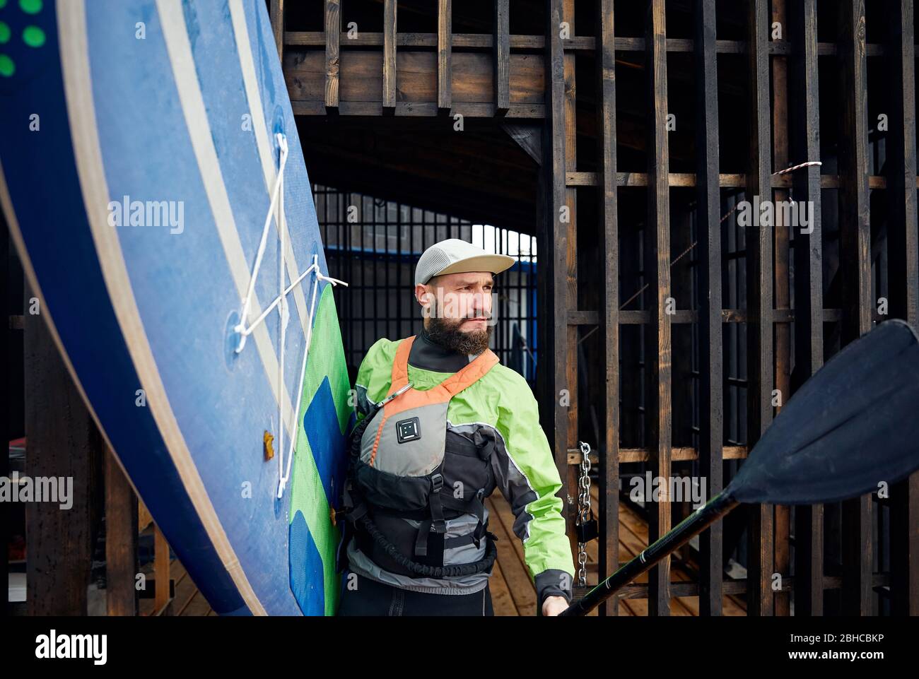 Portrait von bärtigen Athlet im Neoprenanzug holding Surfbrett und Paddel Stockfoto