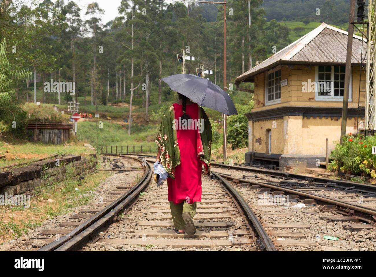 Frau, die traditionelle Sari und schwarzen Schirm zu Fuß auf Bahnstrecken in Sri Lanka. Stockfoto