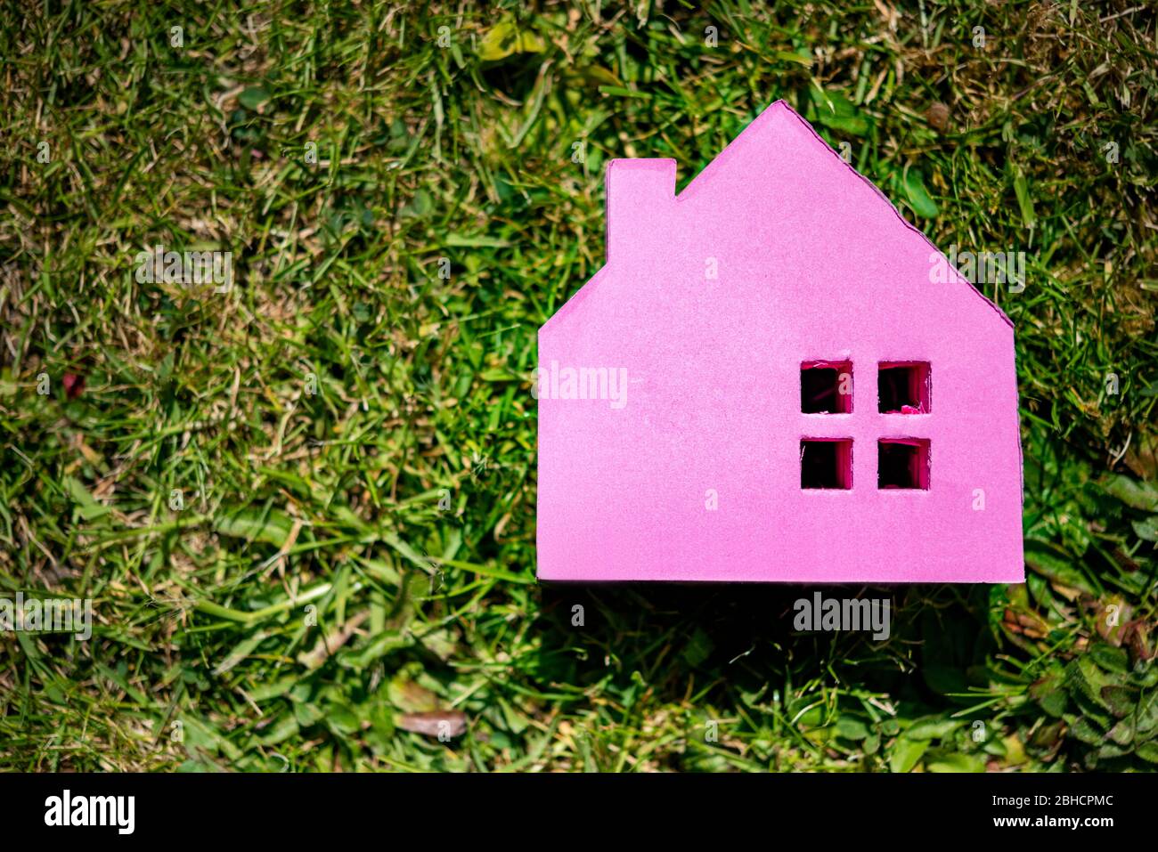 Ein rosa hausförmiger Block auf einem Rasen-Garten-Hintergrund. Immobilienmarktkonzept Stockfoto