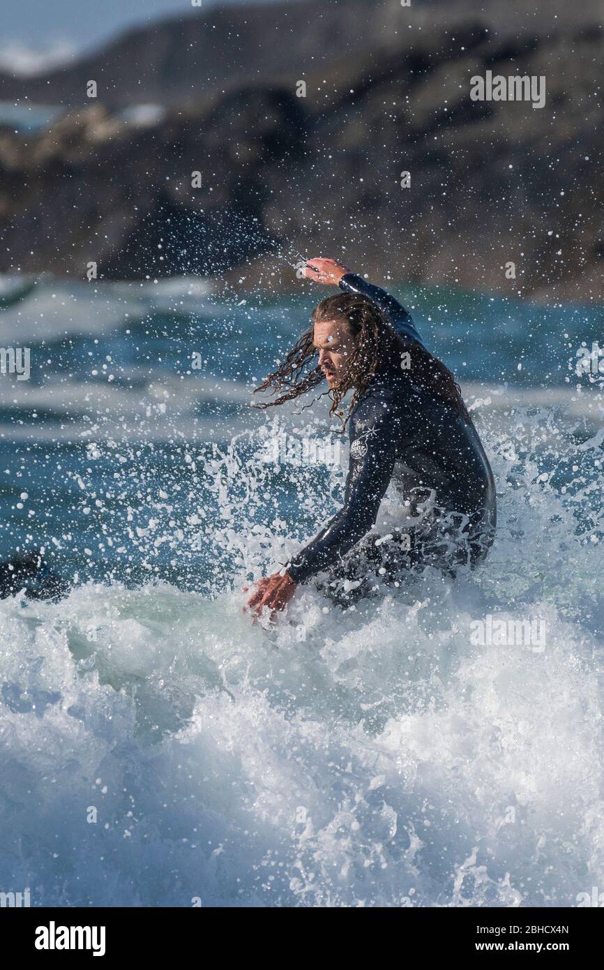 Spektakuläre Action als männlicher Surfer mit langen Haaren reitet eine Welle bei Fistral in Newquay in Cornwall. Stockfoto