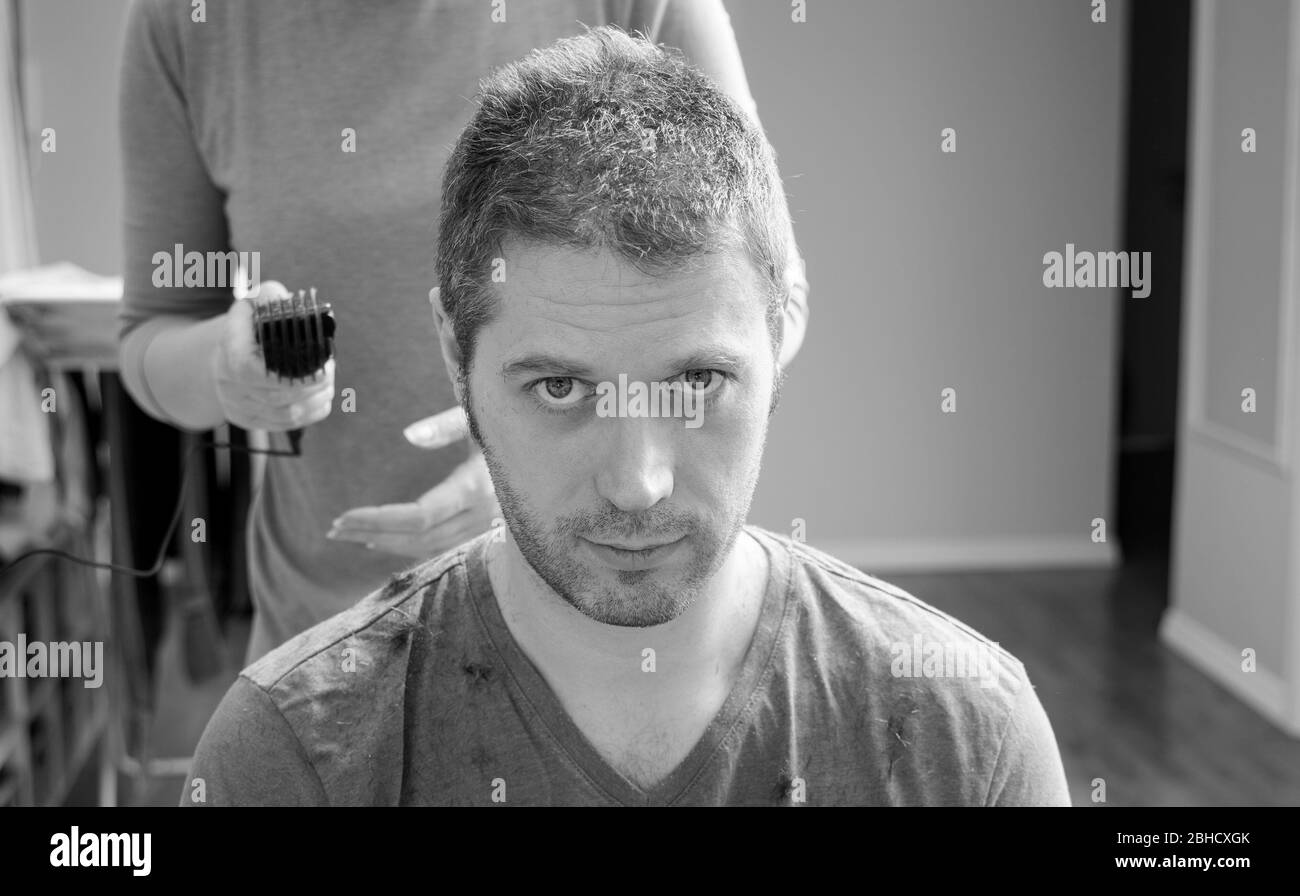 Frau macht Haarschnitt mit Haarschneider zu Mann zu Hause. Schwarzweiß-Foto. Stockfoto