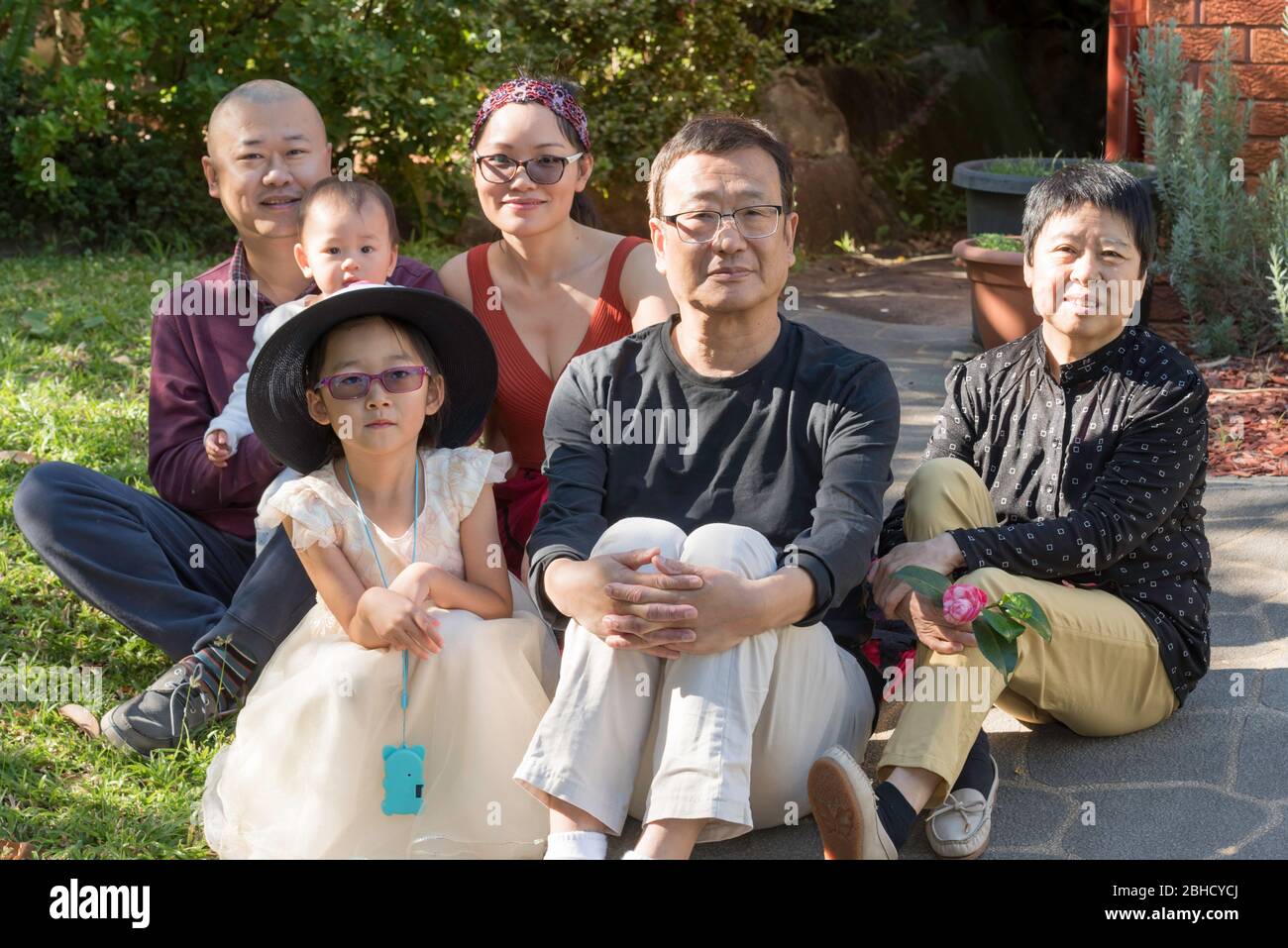 Eine glückliche chinesische Großfamilie, die in Australien lebt, sitzt während der Covid-19-Epidemie auf dem vorderen Weg ihres Sydney-Hauses. Stockfoto