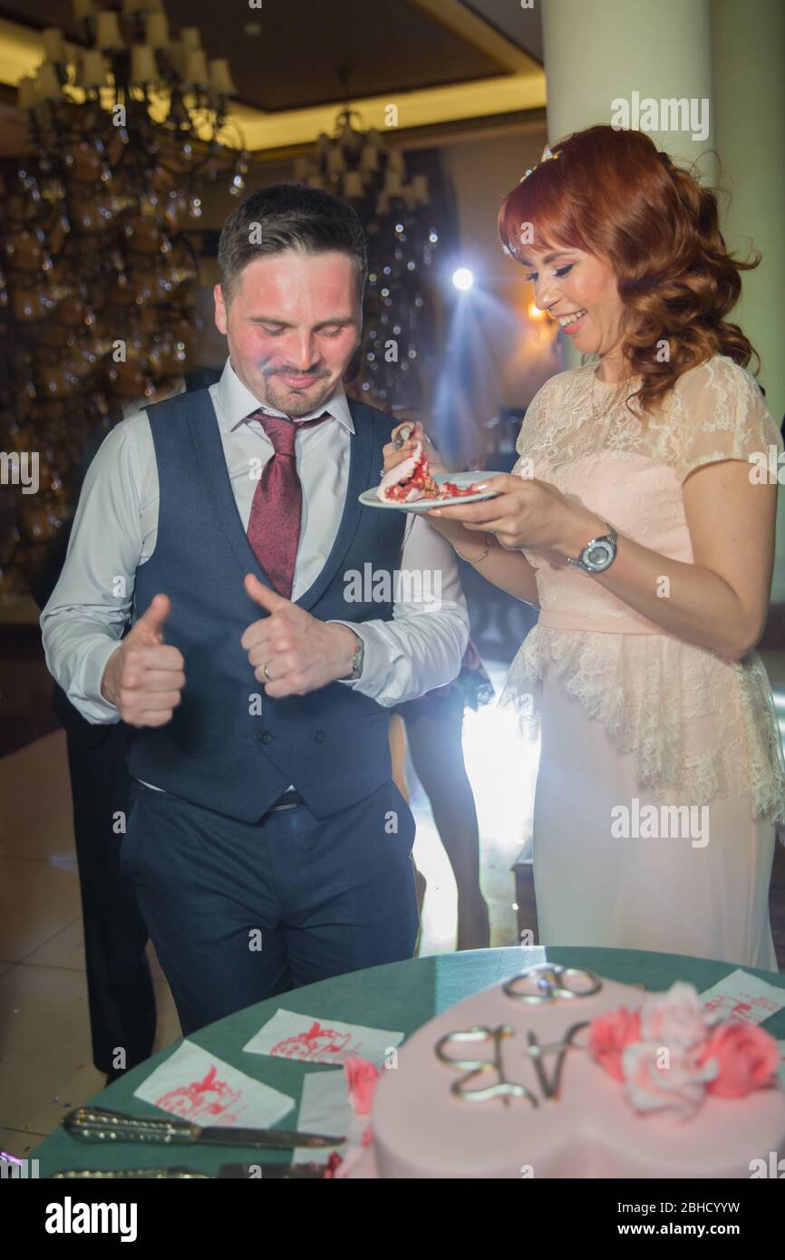 Ein unglaubliches Paar, das Hochzeitstorte isst. Schöne Brautpaar und ihr Mann essen Kuchen und sie lachen zusammen. Baku, Aserbaidschan .7.04.2019 . Stockfoto