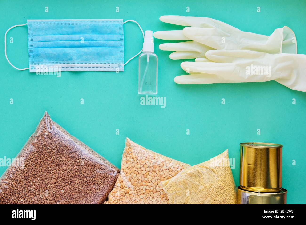Verschiedene Getreidearten und Konserven, neben einer medizinischen Maske und Handschuhen auf blauem Hintergrund. Das Konzept der sicheren Lebensmittelzustellung während der Quarantäne. Stockfoto