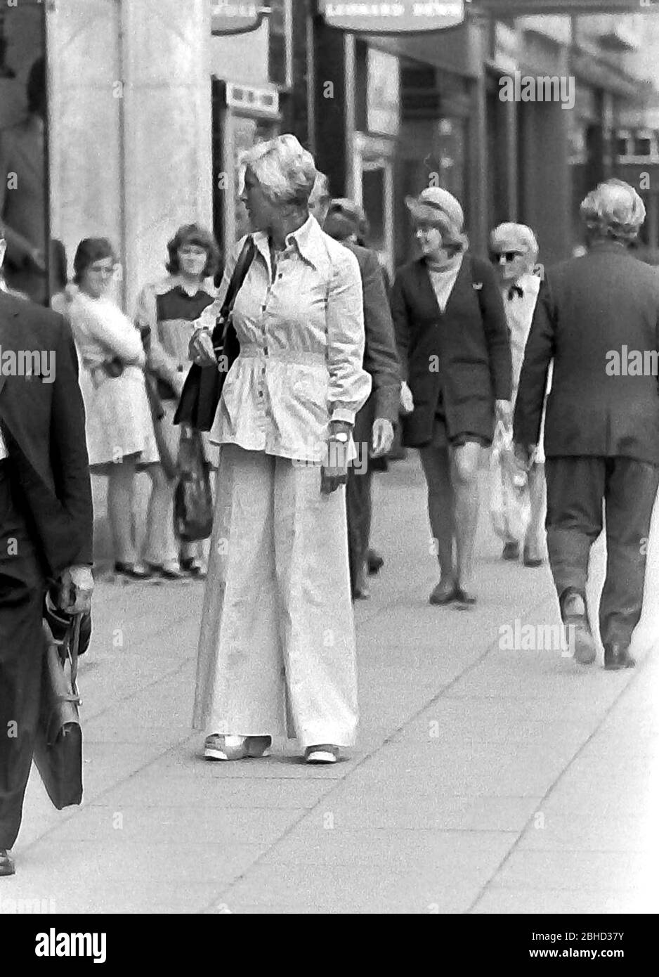Das tägliche Leben auf den Straßen in Manchester, England, Großbritannien im Jahr 1974. Eine elegant gekleidete Frau mit einem Hosenanzug steht auf dem Bürgersteig. Stockfoto