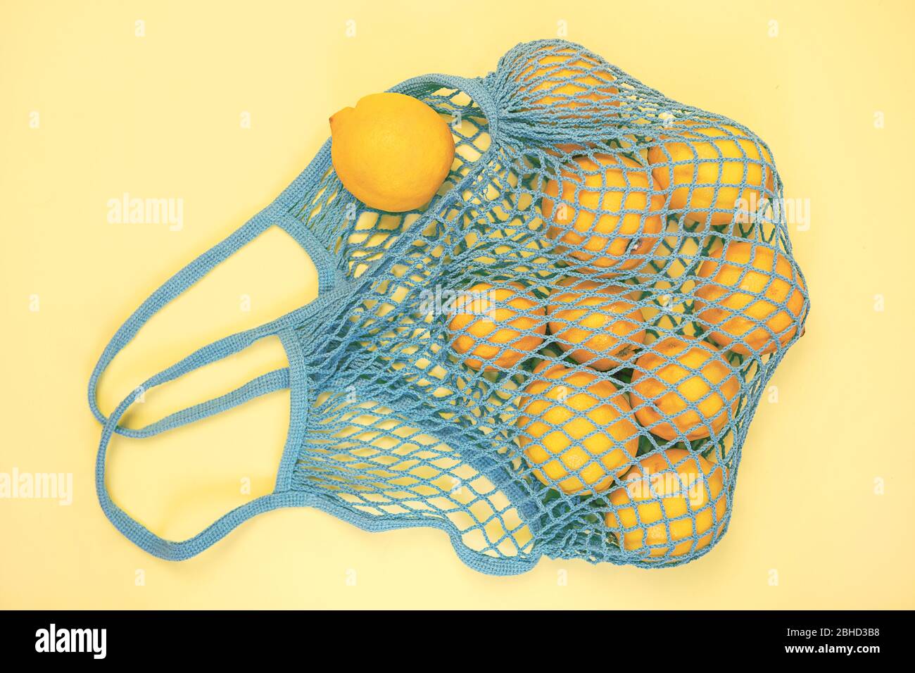 Viel gelbe Zitrone in der blauen Netztasche flach lag auf gelbem Hintergrund. Keine Abfälle, umweltfreundlich, kein Kunststoffkonzept. Zitrusfrüchte. Stockfoto