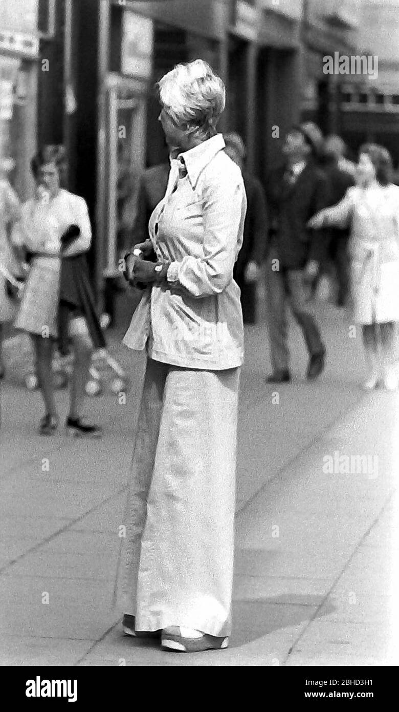 Das tägliche Leben auf den Straßen in Manchester, England, Großbritannien im Jahr 1974. Eine elegant gekleidete Frau mit einem Hosenanzug steht auf dem Bürgersteig. Stockfoto