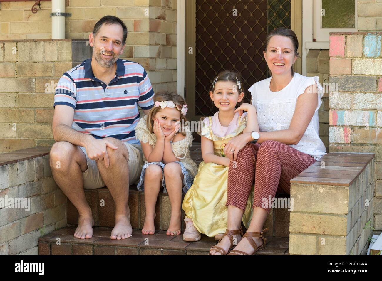 Eine lächelnde simbabwische Familie, die in Australien lebt, sitzt während der Covid-19-Epidemie an der Vordertreppe ihres Hauses in Sydney. Stockfoto