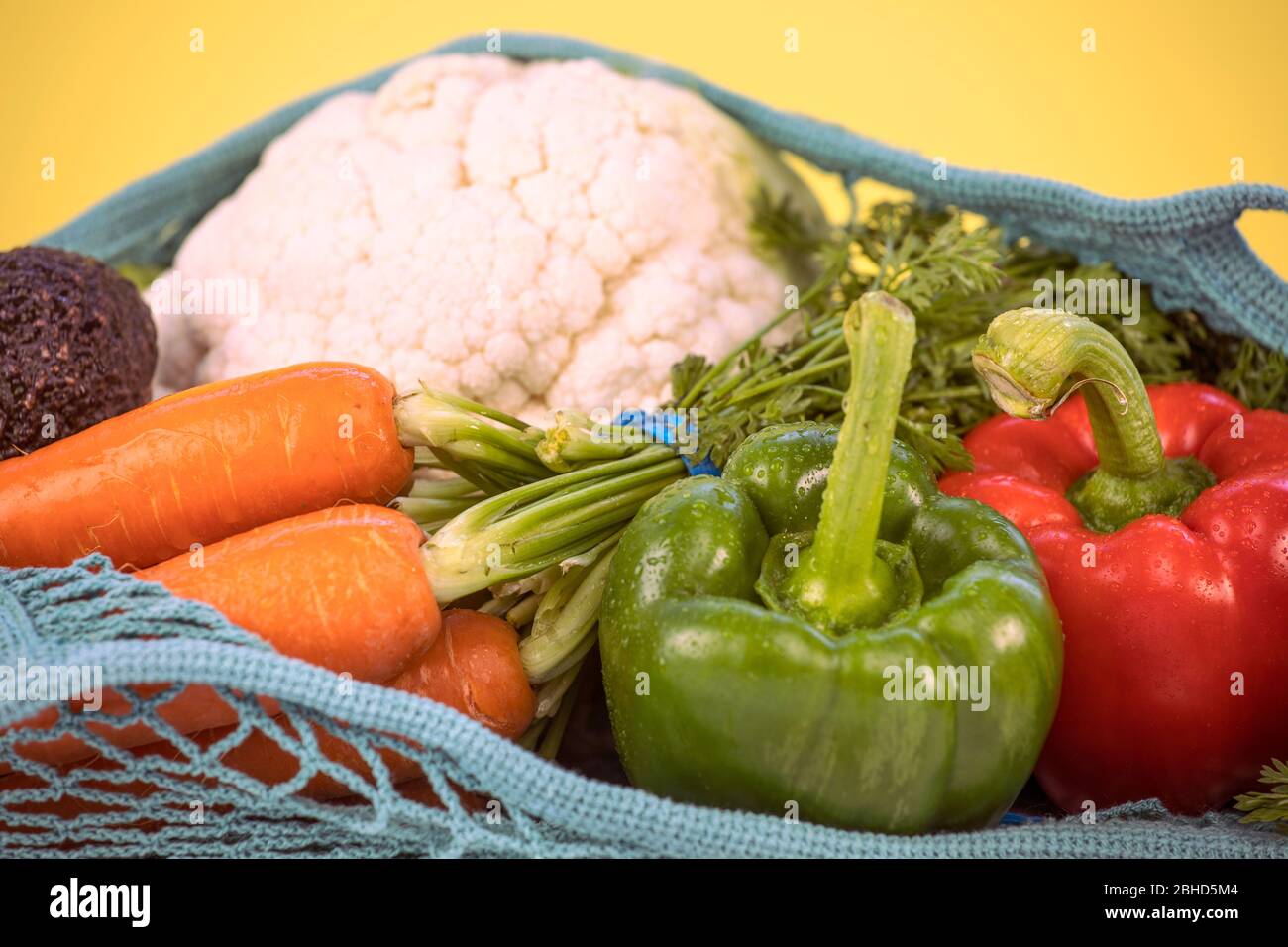 Nahaufnahme von bunten frischen Gemüse in einem Mesh-Tasche, wiederverwendbar, nachhaltig, umweltfreundlich, Kunststoff, Null Abfall Konzept. Verschiedene Gemüse, auf gelb Stockfoto