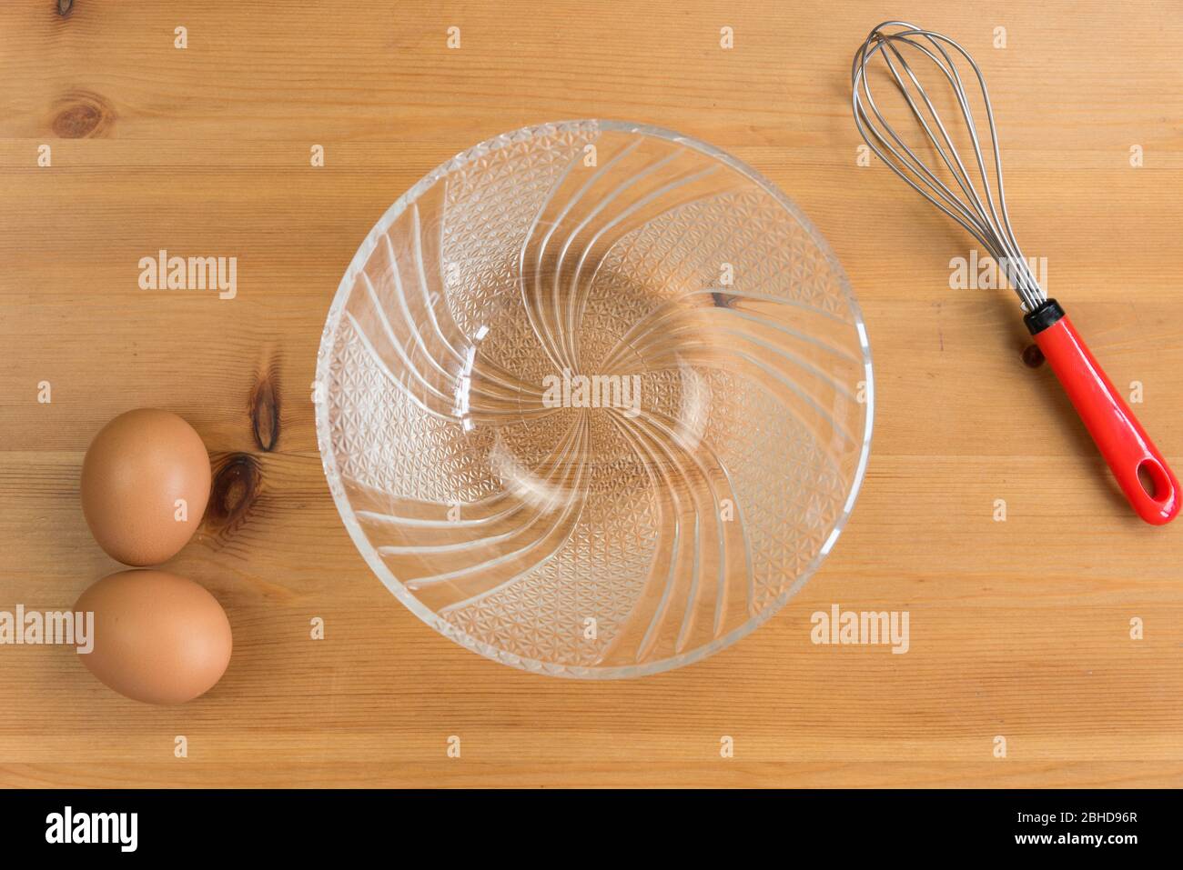 Zwei braune Eier, ein Schneebesen und eine Kristallschale auf einem Holztisch. Stockfoto
