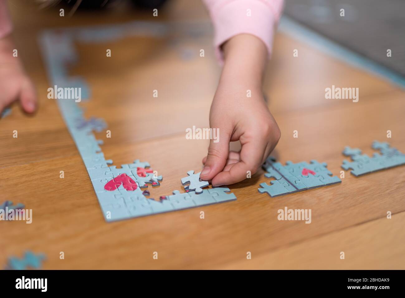 Blonde Mädchen in einem rosa Pullover mit einem Puzzle auf dem Boden durch die Einengung von Coronavirus covid-19 spielen Stockfoto