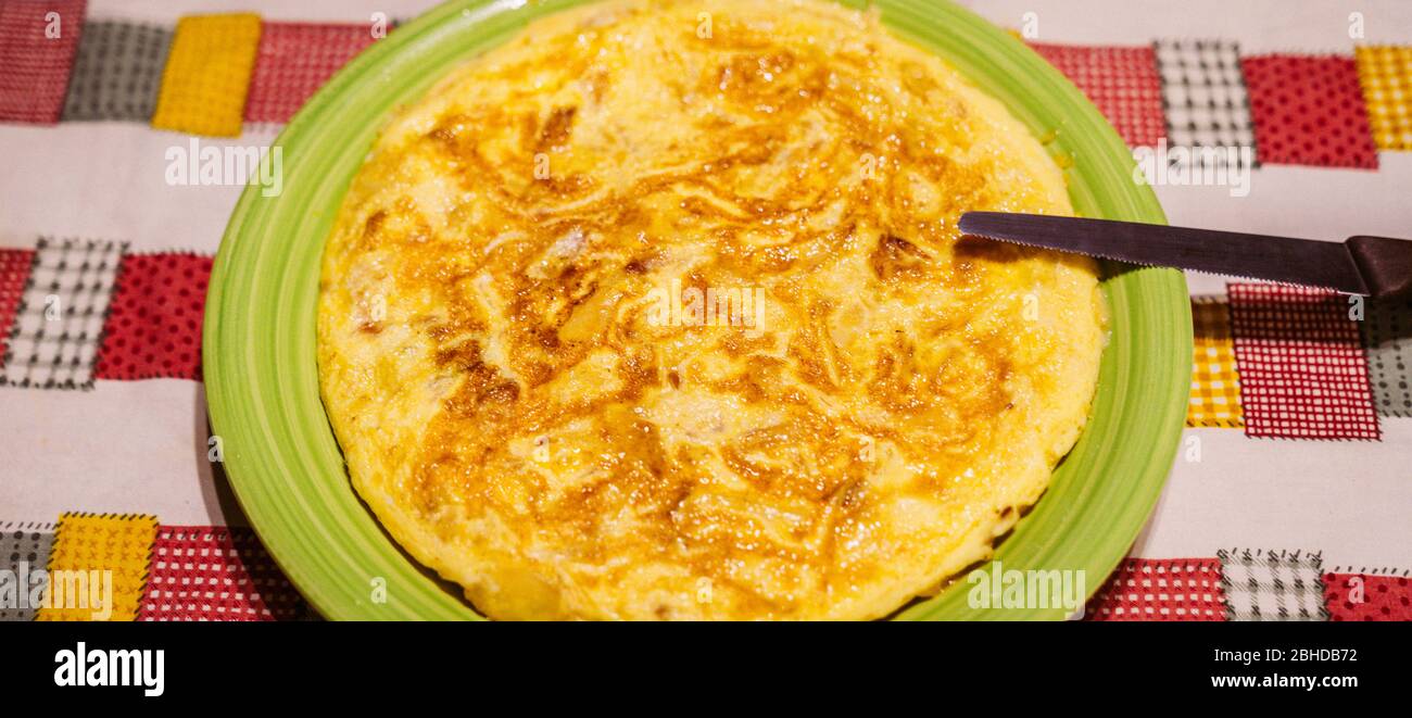 Leckere spanische Tortilla auf einem grünen Teller mit einem Messer, um die Portionen auf einem Tisch mit einer Familie Tischdecke geschnitten. Gelbes Omelett mit Eiern, Kartoffeln und auf Stockfoto