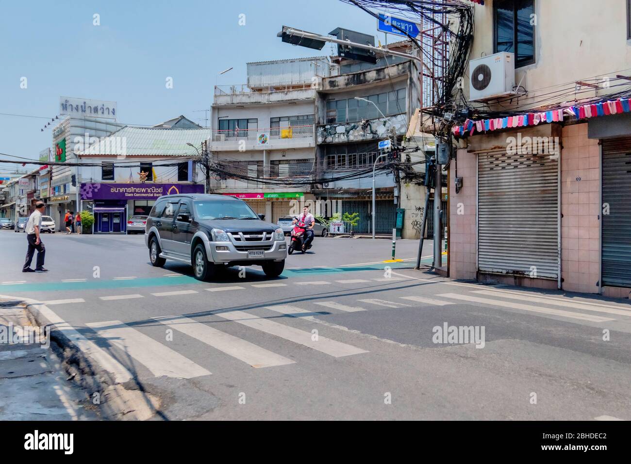 Das silberne Auto fährt auf der Straße und ein alter Mann überquert die Straße ohne Pflaster in Bangkok, Thailand 14. April 2018 Stockfoto