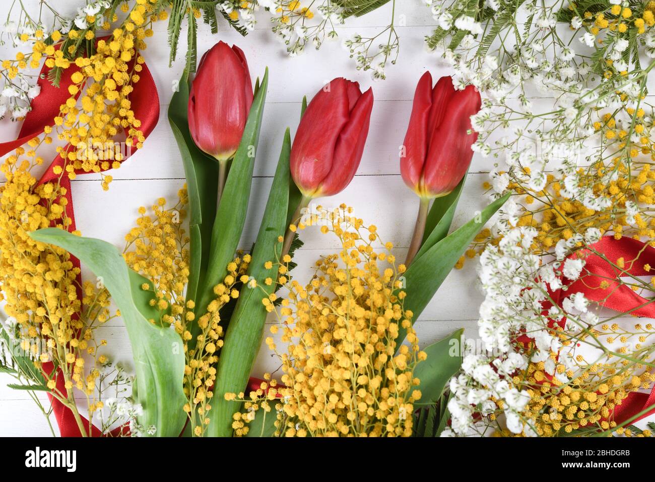 Floraler Hintergrund, Frühlingskonzept, weißes Holzbrett, rotes Band, Frühlingsblumen wie gelbe Mimosa. Platz für Text, kopieren Raum in der Mitte, Mitte Stockfoto