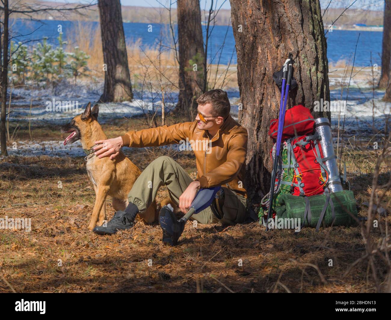Ein Mann mit einer Prothese ruht nach einem langen Spaziergang mit seinem besten Freund - einem Hund aus einem Tierheim. Freundschafts- und Unterstützungskonzept Stockfoto