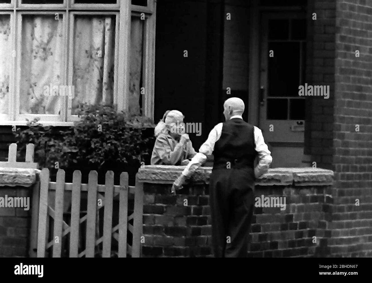 Das tägliche Leben auf den Straßen in Manchester, England, Großbritannien im Jahr 1974. Ein älterer Mann und eine ältere Frau plaudern am Gartentor eines Hauses. Stockfoto