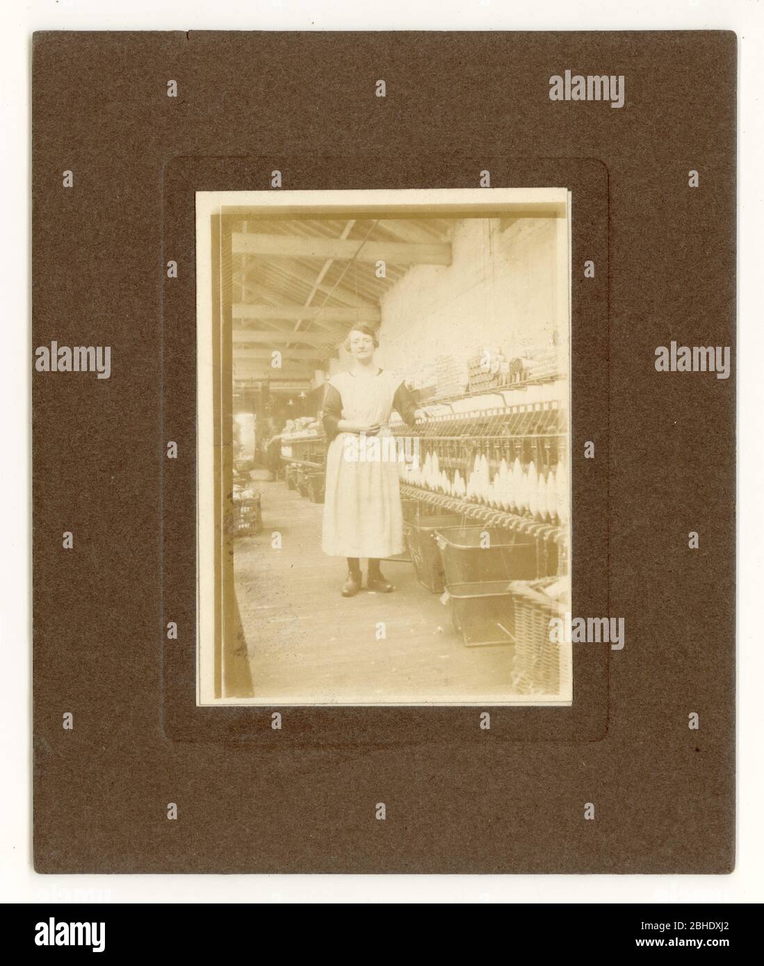 Anfang des 20. Jahrhunderts Fotografie von Lancashire Baumwollspinner, neben einem Spinnmuli in einer Baumwollfabrik stehend, trägt Clogs, Radcliffe, Lancashire, Großbritannien um 1915 Stockfoto