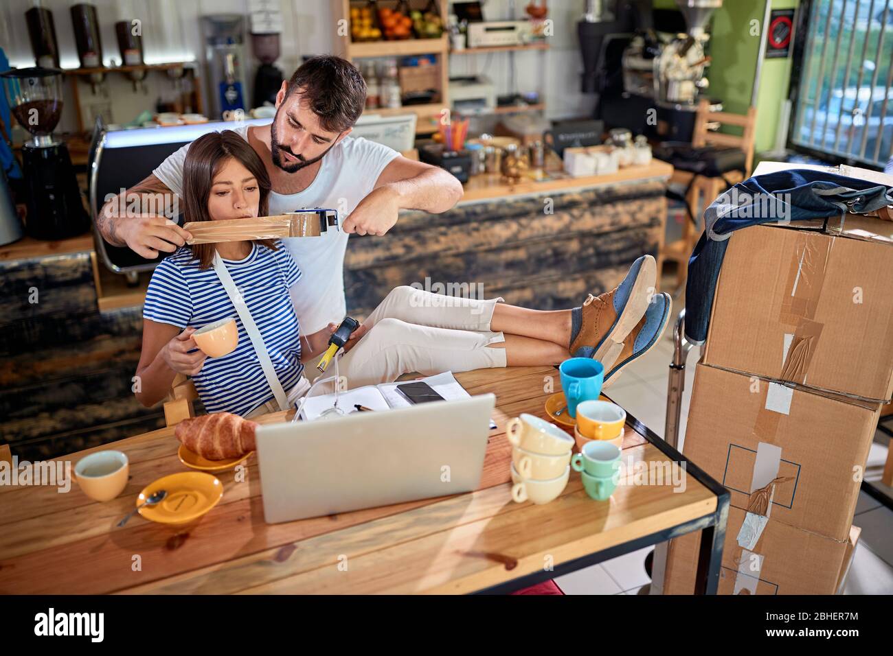 Der junge Mann legt ein Klebeband über den Mund der Frau, scherzt, wie sie zu viel reden. Junge Paar scherzt in neuen ungeöffneten Café ihrer eigenen. Neuer BU.-Start Stockfoto