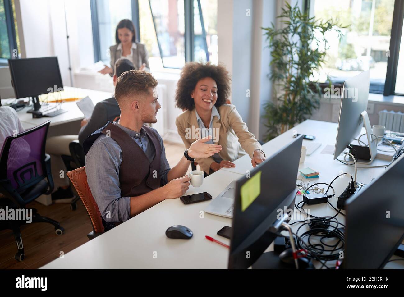 Ein männlicher Kollege erklärt einer anderen weiblichen Kollegin Inhalt von einem Monitor in modernen Open Space Office. Casual modernen Business Stockfoto