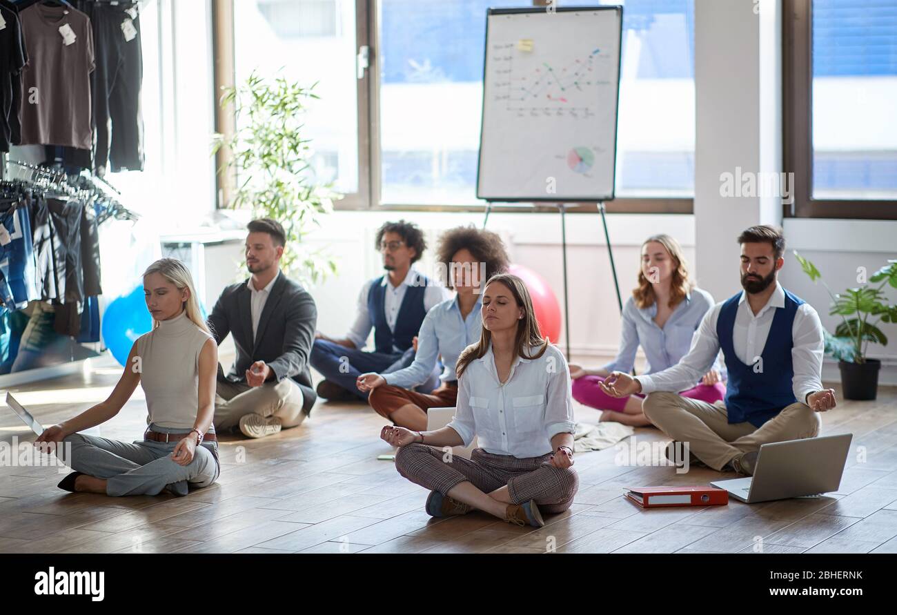 Gruppe von Geschäftskollegen meditieren bei der Arbeit, sitzen auf dem Boden. Modern, Business, Meditation Konzept Stockfoto