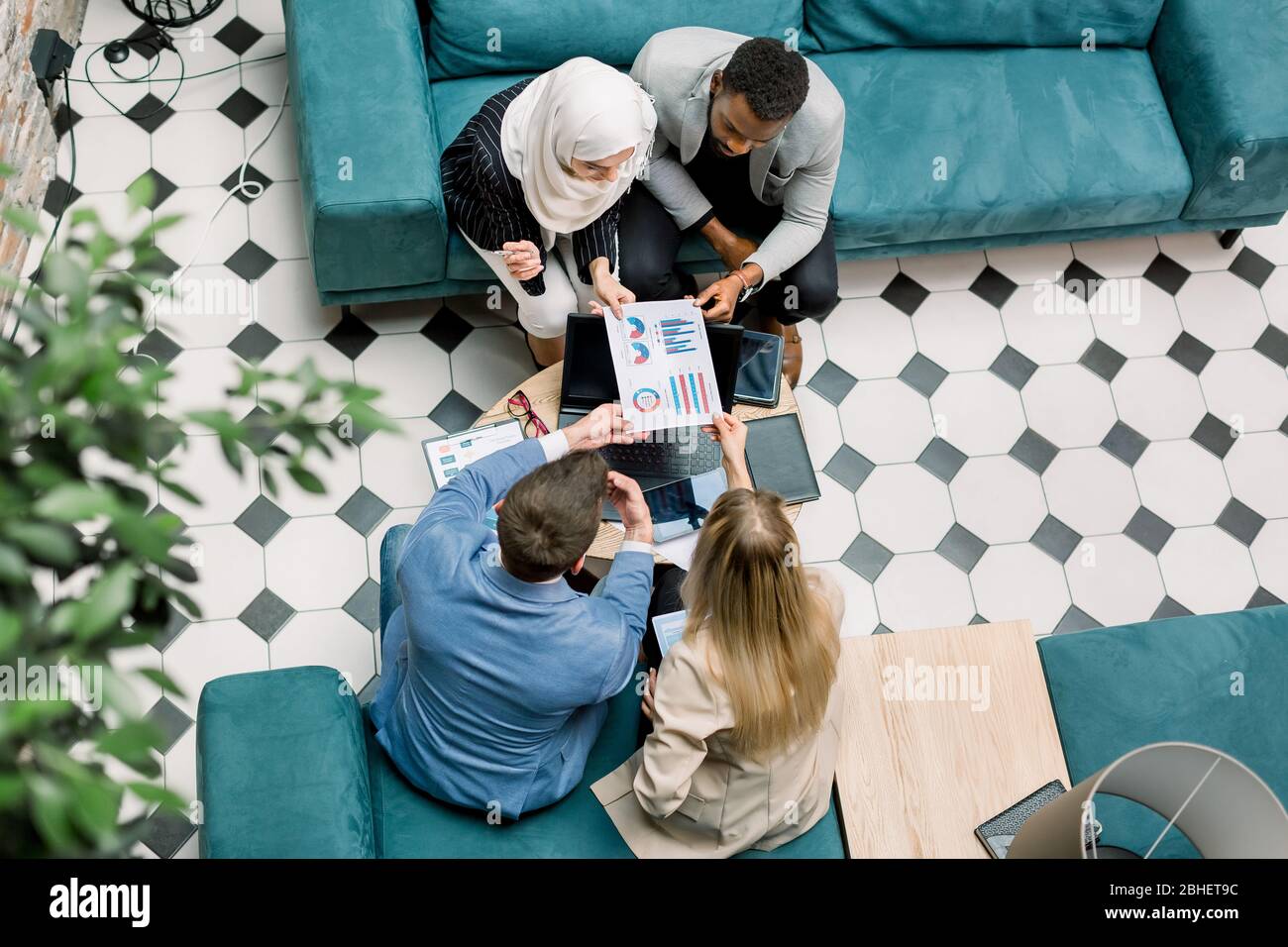 Draufsicht auf vier junge Geschäftsleute verschiedener Nationalitäten, die mit Finanzdokumenten arbeiten und zusammen Grafiken und Diagramme betrachten, sitzen Stockfoto