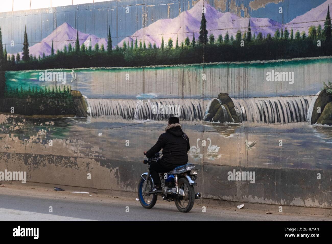 Ein Motorradfahrer fährt in Qamischli, Nordostsyrien, an einem utopischen Wandgemälde vorbei. Stockfoto