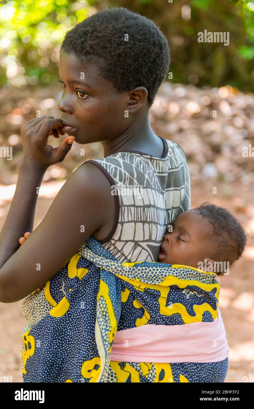 Frau, die das Baby auf dem Rücken trägt, beobachtet die Begrüßungszeremonie des Chefs im Heiligen Wald von Kpassè Zoun in Ouidah, Benin. Stockfoto