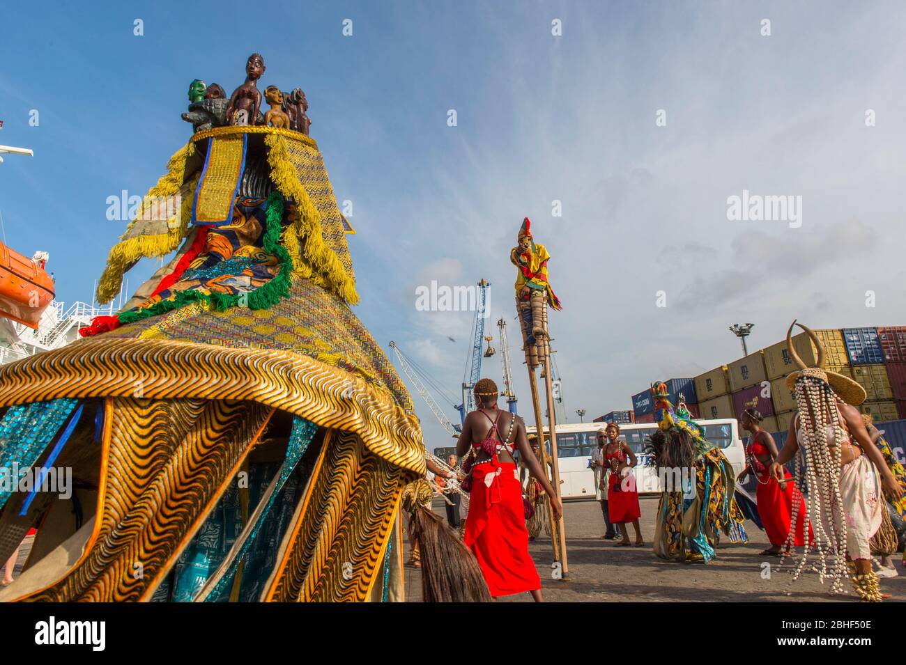 Kulturelle Aufführung mit Tänzen und einem Mann auf Stelzen im Hafen von Lome, Togo. Stockfoto