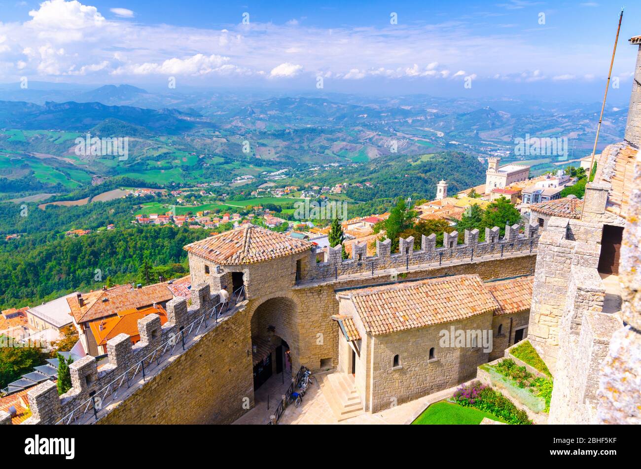 Republik San Marino, 18. September 2018: Luftbild von oben Landschaft mit Tal, grünen Hügeln, Feldern, Dörfern von Vorstadtviertel, blauer Himmel Hintergrund und Stein Festung Wand und Turm mit Merlonen Stockfoto