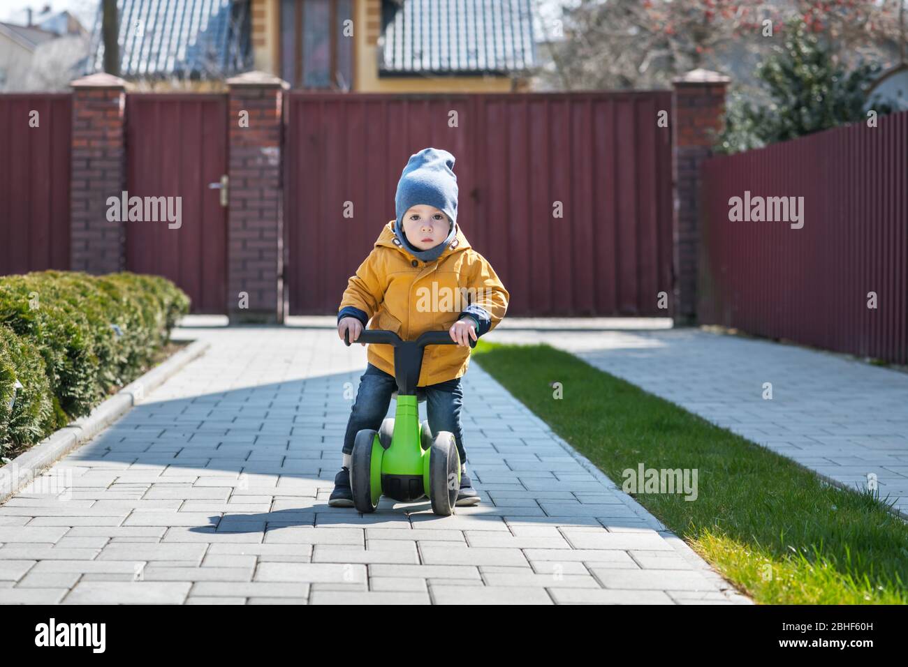 Kleiner Junge auf seinem Fahrrad auf Pflasterweg in der Nähe seines Hauses. Happy Kindheitkonzept Stockfoto