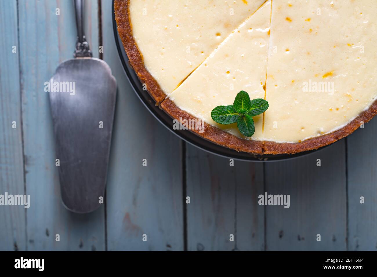 Flugzeug runden klassischen New York Käsekuchen und seine Scheibe mit Zweig Minze auf einem Teller auf einem Holztisch. Das Konzept der Bäckerei und Süßspeisen Desserts Stockfoto