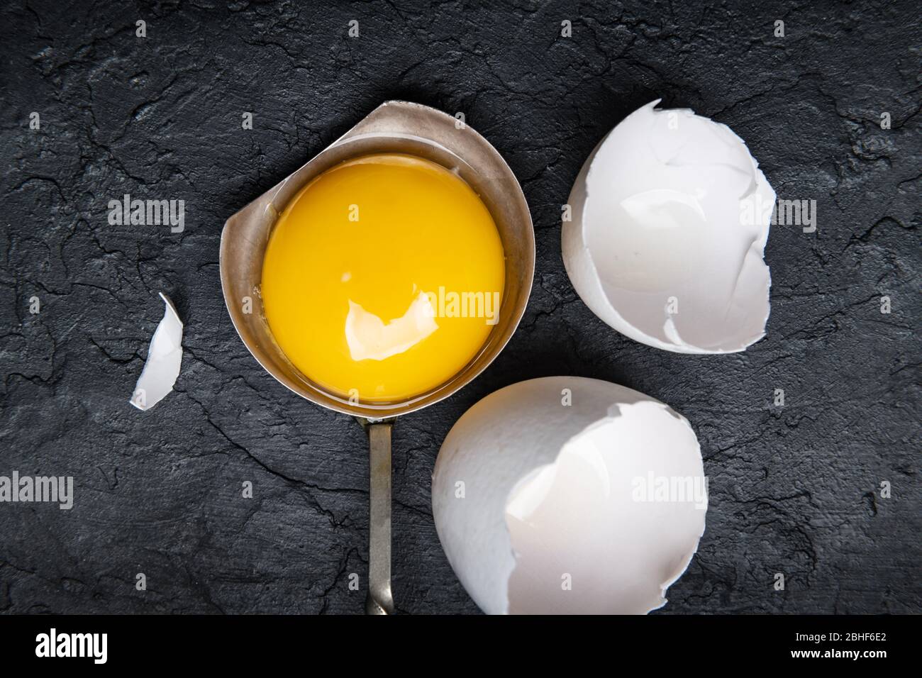 Hühnerdotter aus gebrochenem Bio-Ei in silbernem Löffel auf schwarzem Beton Hintergrund. Food-Fotografie Stockfoto