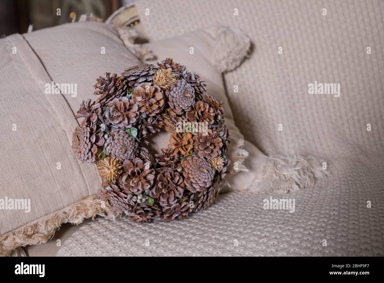 Goldener Weihnachtskranz aus verschiedenen natürlichen Zapfen auf beigem Hintergrund. Kreativer ländlicher Kranz mit Tannenzapfen, Kräutern. Seasons Grußkarte. Kopieren Stockfoto