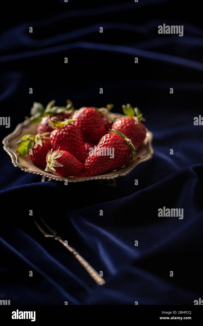 Frische rote Erdbeeren auf einem silbernen Teller auf dunkelblauem Samt Stockfoto