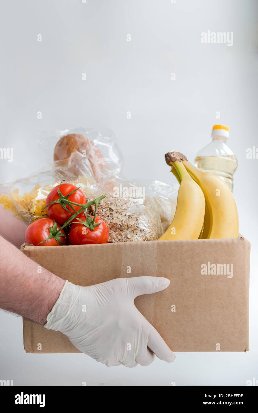 Mann in Gummihandschuhen hält die Schachtel mit Essen. Spende Lieferung von Lebensmitteln Stockfoto