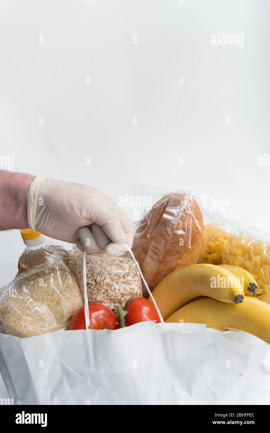 Mann in Gummihandschuhen hält die Papiertüte mit Lebensmitteln. Spende Lieferung von Lebensmitteln Stockfoto