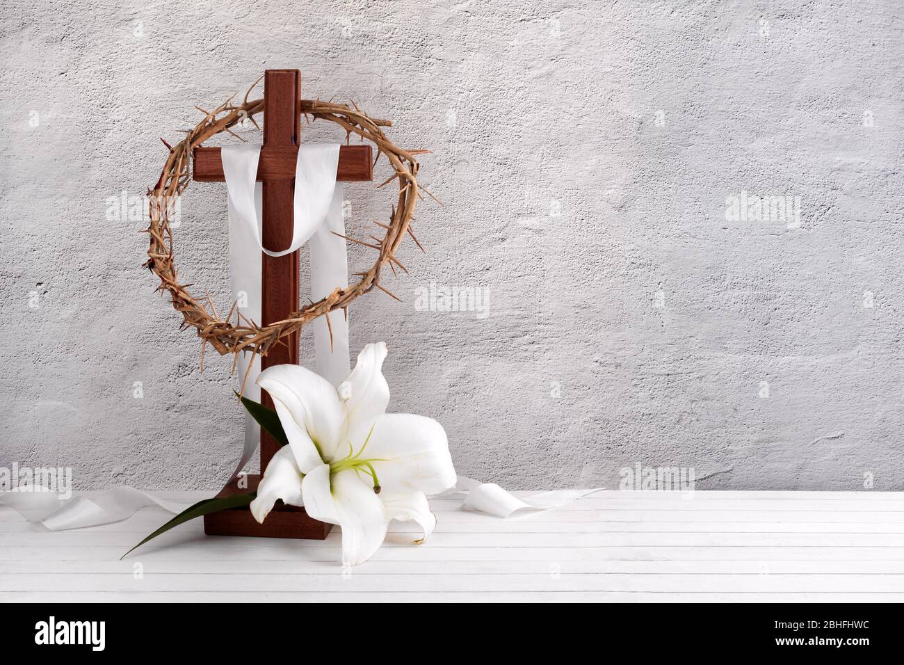 Komposition mit Dornenkrone, Holzkreuz und Lilie auf hellem Hintergrund Stockfoto
