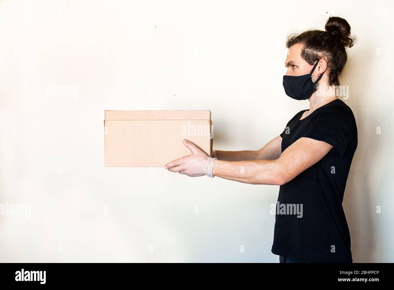 Liefermann, der Pappkartons in medizinischen Handschuhen und Schutzmaske gibt. Online-Shopping und Express-Lieferung während der Quarantäne Stockfoto