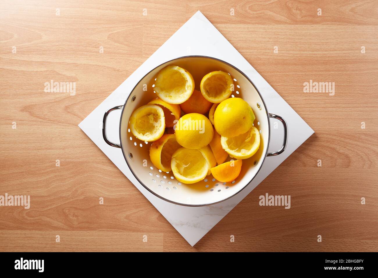 High-Angle-Aufnahme eines Collnders mit Zitronenhälften gefüllt Reste von der Herstellung von hausgemachten Limonade, auf einem Holztisch und weißen Marmorfliesen. Stockfoto