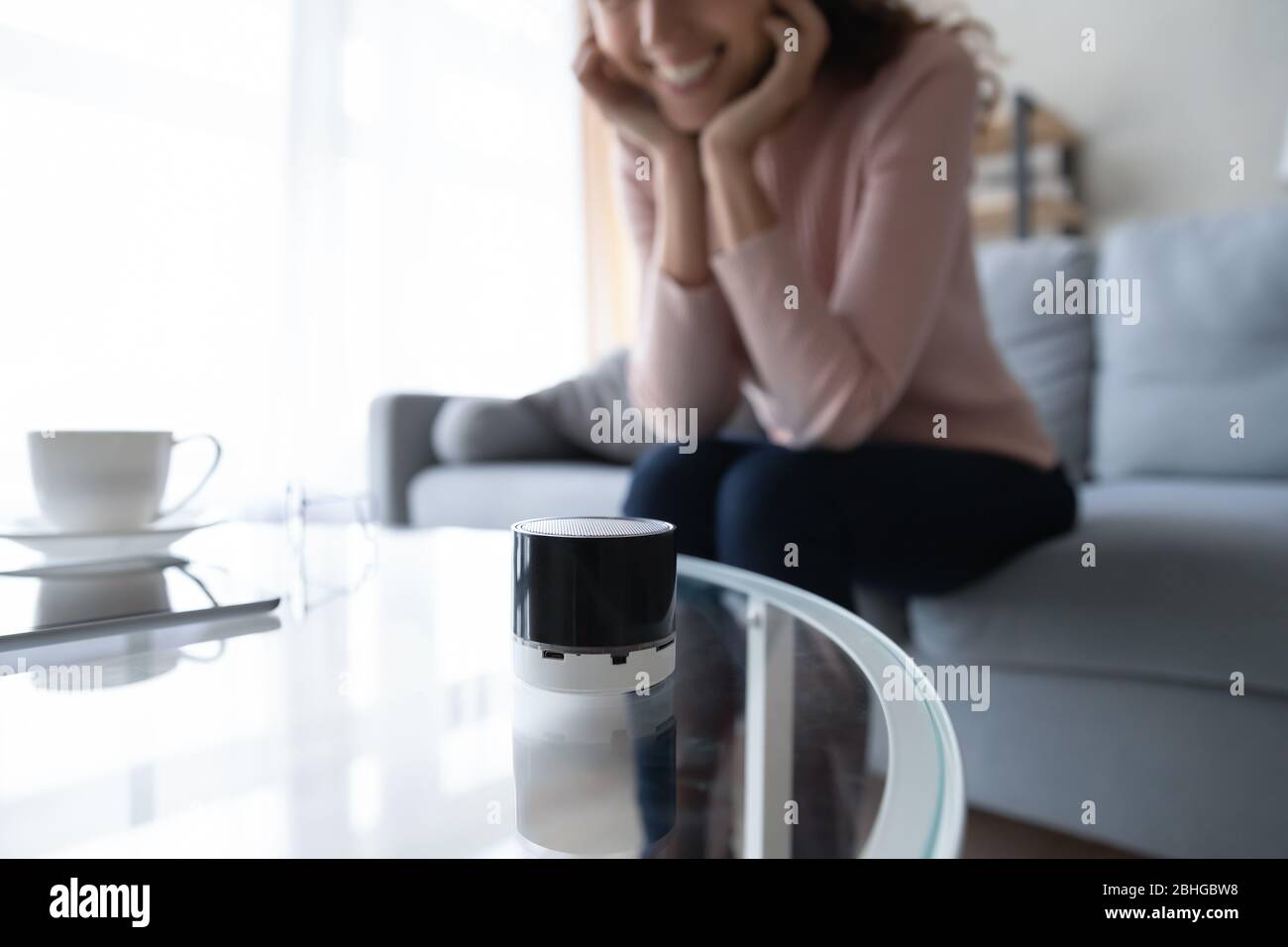 Glückliche Frau, die auf kompakten Sprachassistenten auf Glastisch schaut. Stockfoto