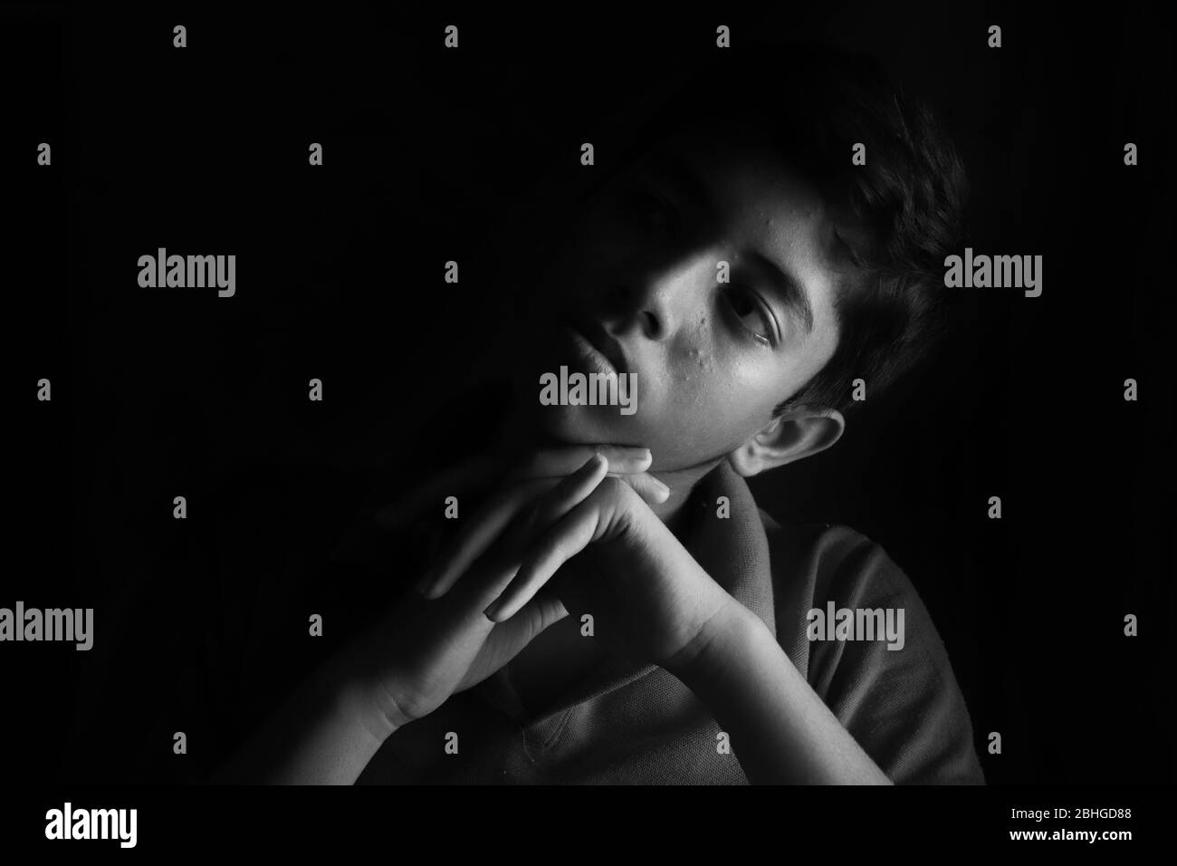 Porträt eines gestressten asiatischen Jungen vor schwarzem Hintergrund. Ein indischer melancholischer Junge denkt. Traurigkeit Ausdruck eines asiatischen Jungen. Stockfoto