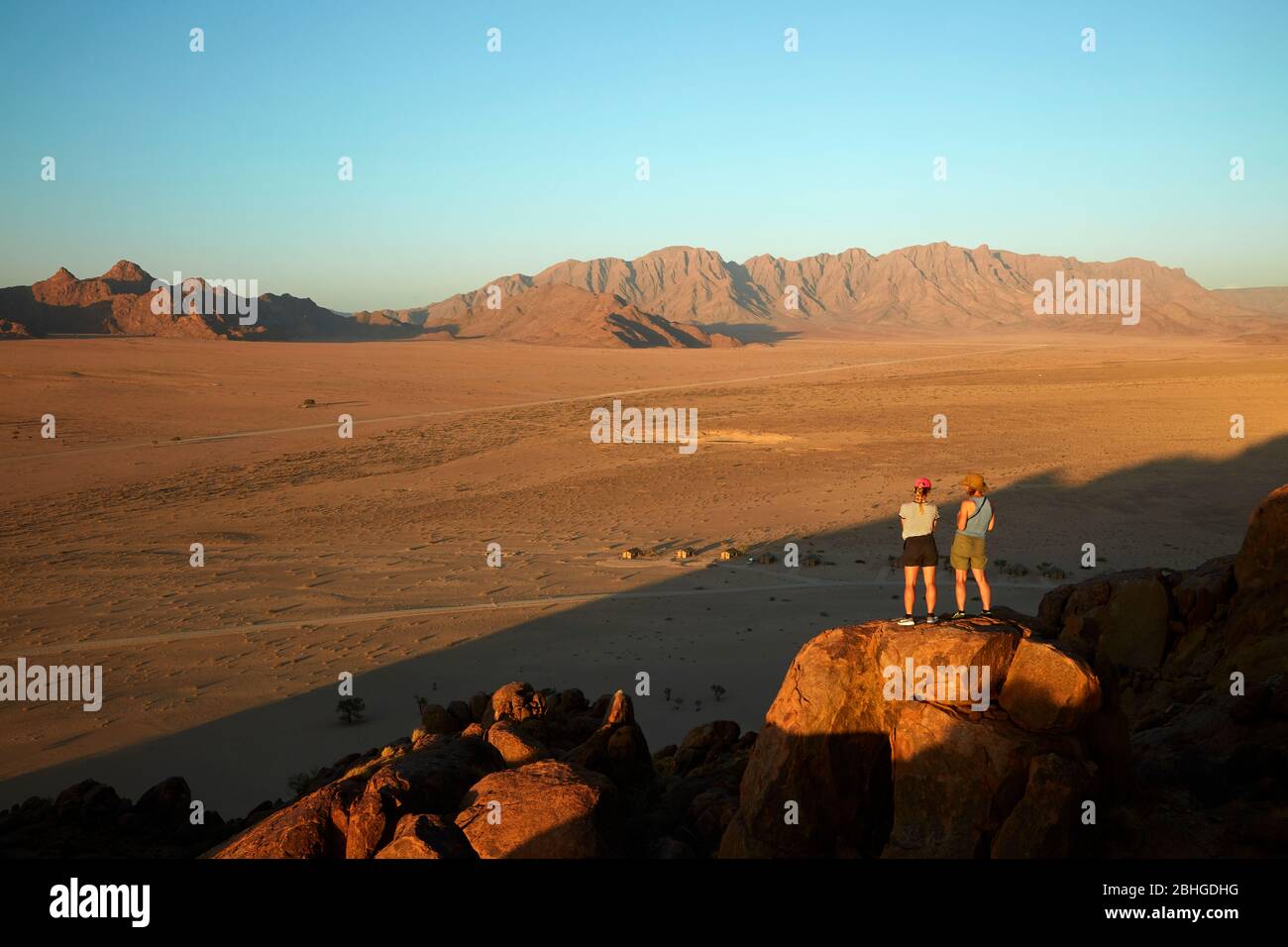 Frauen mit Blick auf Berge und Desert Camp, von oben auf einem Felsen Koppie, Sesriem, Namib Desert, Namibia, Afrika (Modell veröffentlicht) Stockfoto