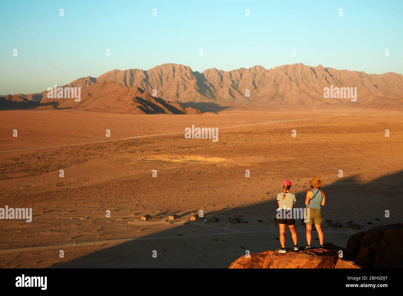 Frauen mit Blick auf Berge und Desert Camp, von oben auf einem Felsen Koppie, Sesriem, Namib Desert, Namibia, Afrika (Modell veröffentlicht) Stockfoto