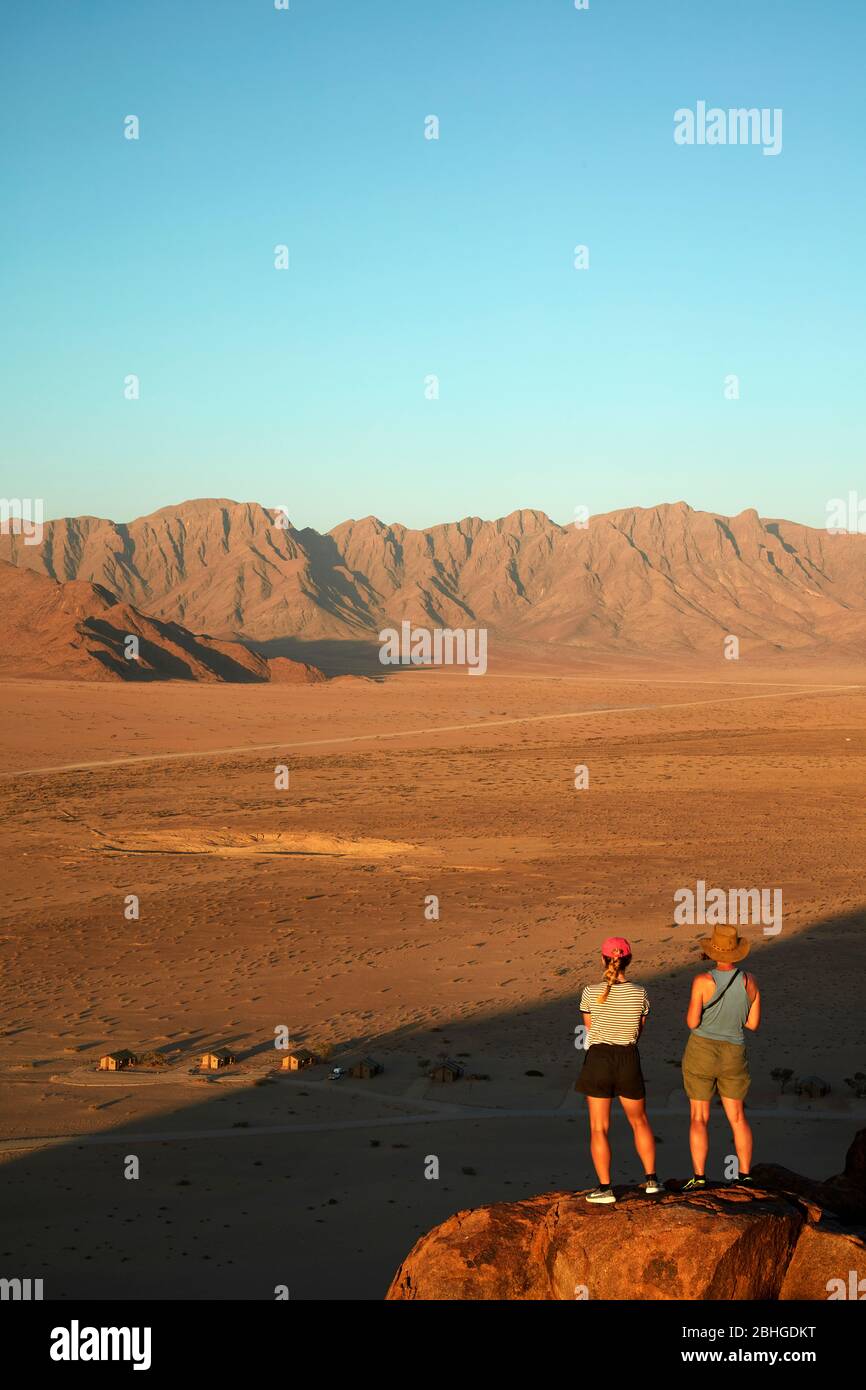 Frauen mit Blick auf Berge und Desert Camp, von oben auf einem Felsen Koppie, Sesriem, Namib Desert, Namibia, Afrika (Modell veröffentlicht) Stockfoto