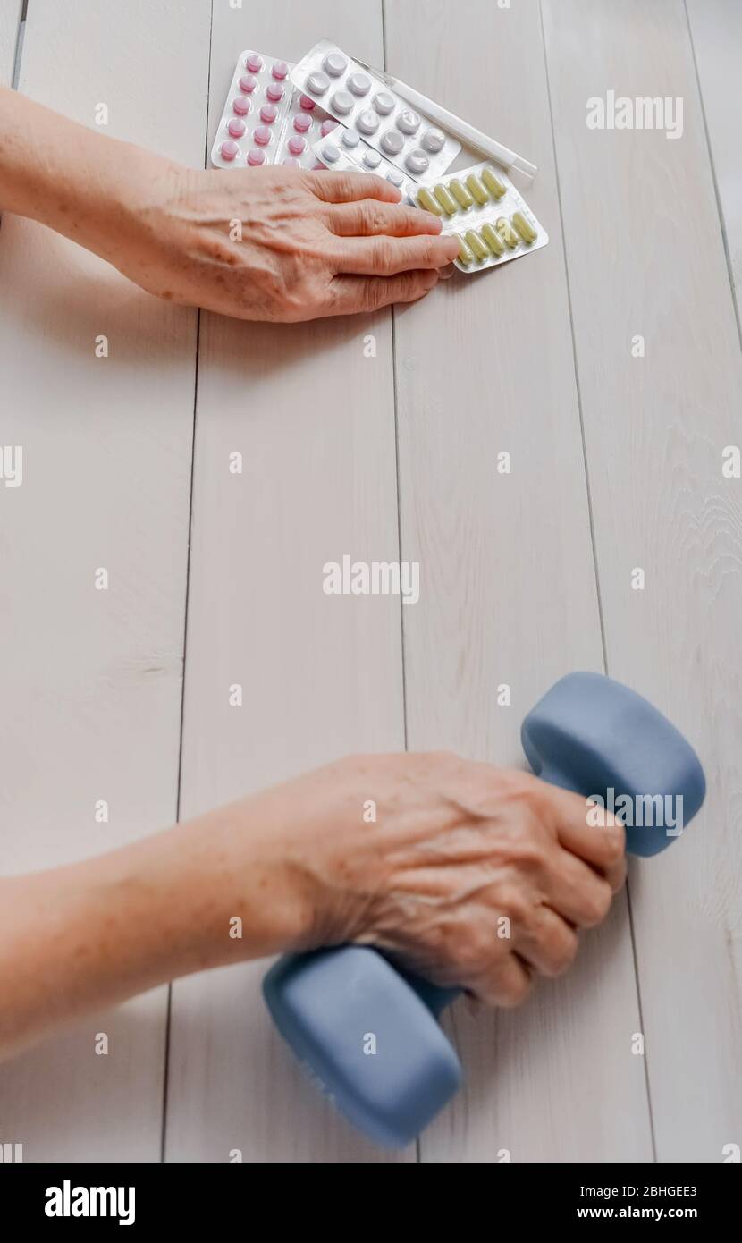 Ältere Hände mit Pillen, Medikamente auf dem Tisch, Glocke. Frau runzelte Hände, Thermometer, bunte Tabletten und stumpfe Glocke, Holzhintergrund. Gesundheitswesen Stockfoto