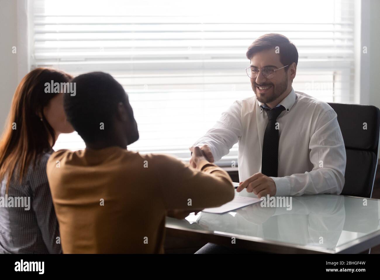Lächelnder Geschäftsmann im Anzug, der sich die Hände mit einem afroamerikanischen Mann schüttelt. Stockfoto